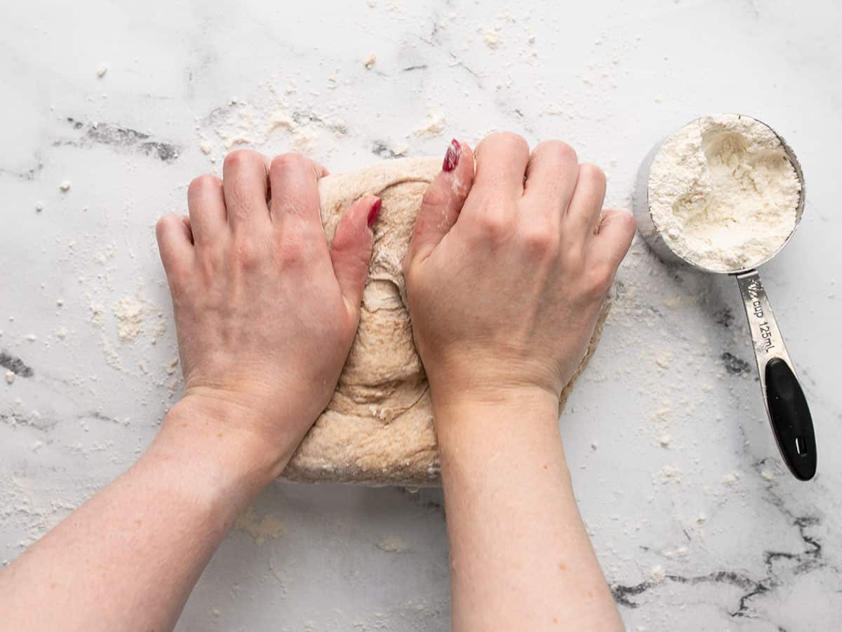 Dough being kneaded with a measuring cup of flour on the side.