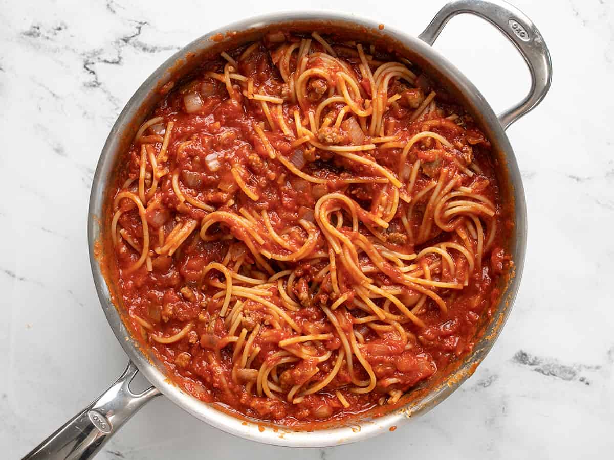 Spaghetti stirred into the meat sauce in the skillet.