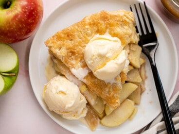 Overhead shot of a slice of apple pie on a white plate with vanilla ice cream and drizzled with caramel sauce.