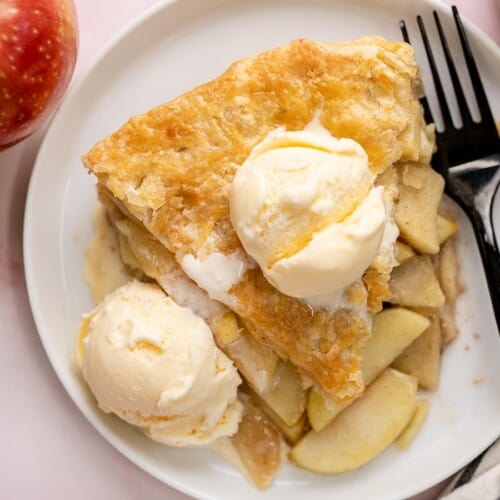 Overhead shot of a slice of apple pie on a white plate with vanilla ice cream and drizzled with caramel sauce.