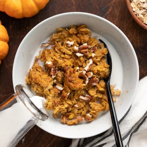 Milk being poured into a bowl of pumpkin pie oatmeal with nuts.