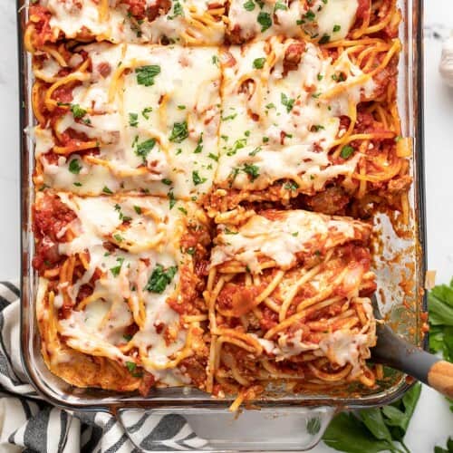 Overhead view of a slice of baked spaghetti being lifted out of the casserole dish.