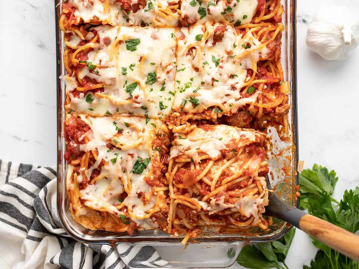 Overhead view of a slice of baked spaghetti being lifted out of the casserole dish.