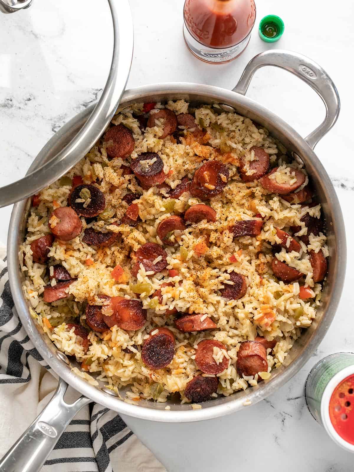 Overhead view of a sausage and rice skillet with hot sauce on the side.