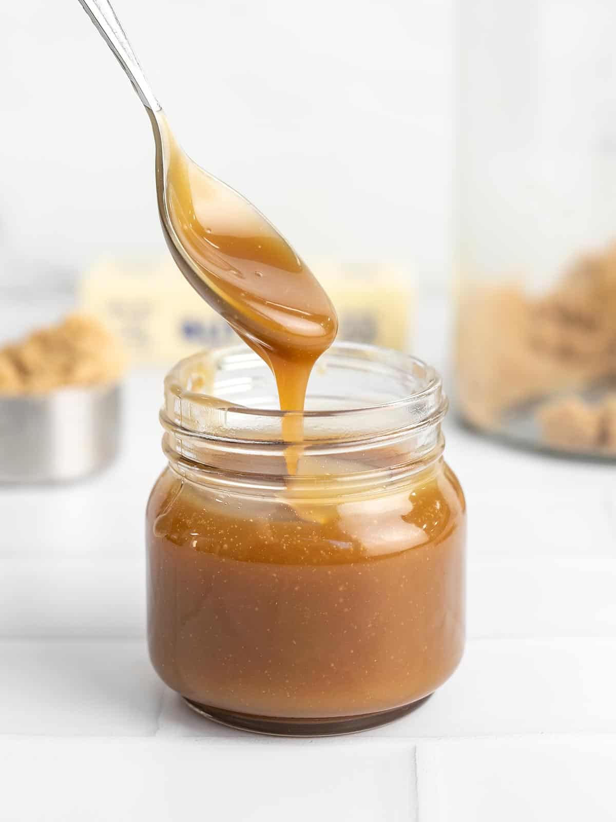 Side shot of a spoon drizzling caramel sauce in a mason jar.