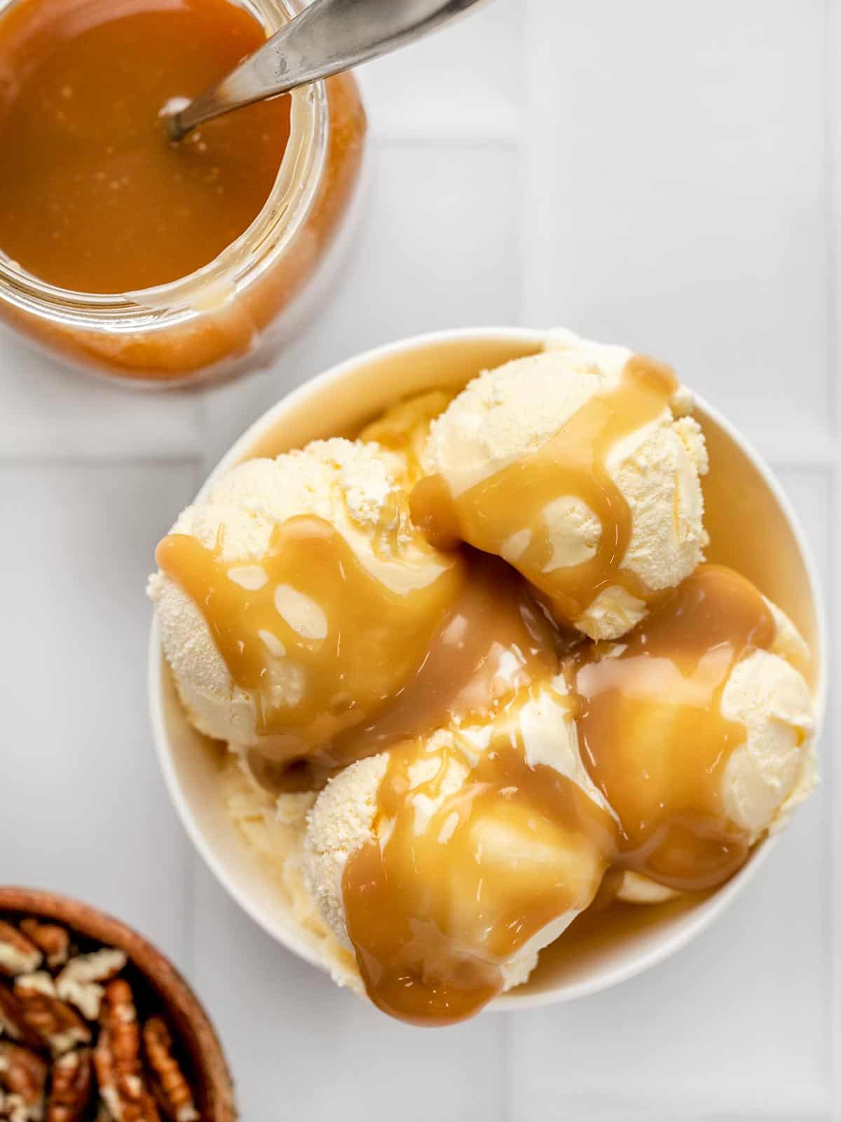 Overhead shot of caramel sauce on vanilla ice cream in a white bowl.