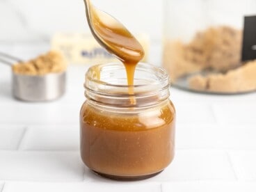 Side shot of a spoon drizzling caramel sauce in a mason jar.