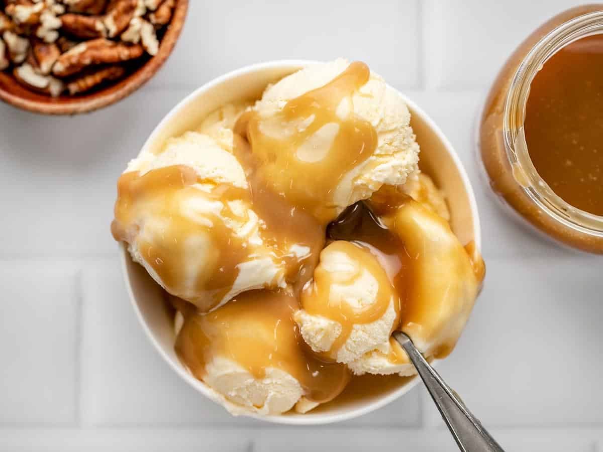 Overhead shot of caramel sauce on vanilla ice cream in a white bowl.