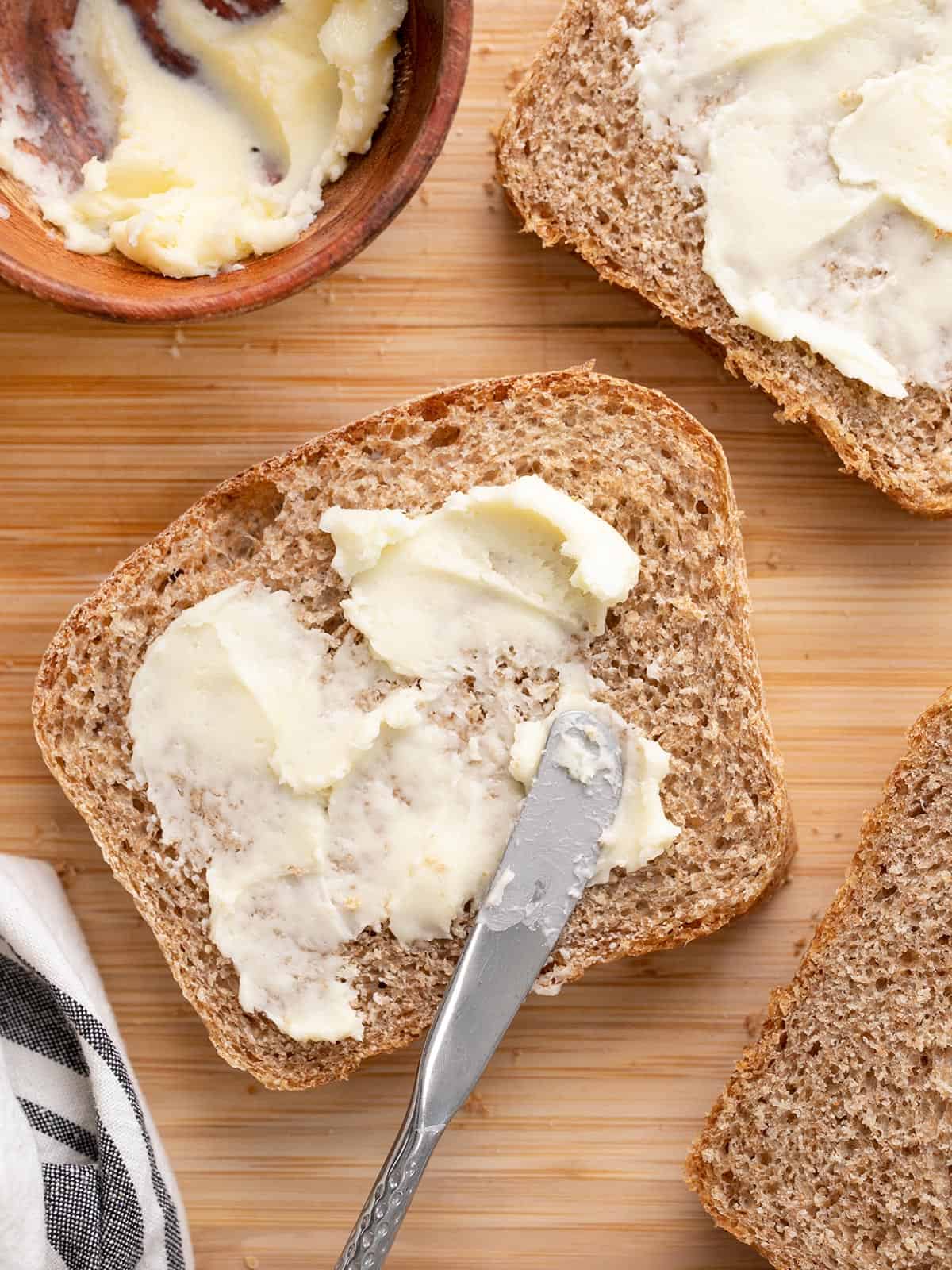 Overhead view of butter being spread on slices of bread.