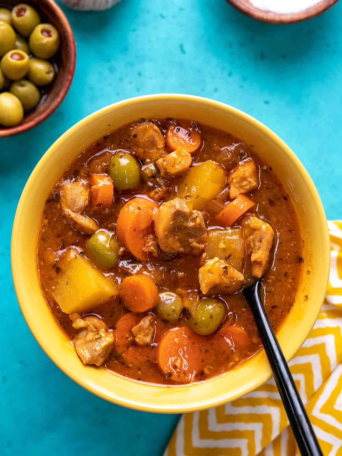 Overhead shot of Guisado de Pollo in a yellow bowl with a spoon in it.