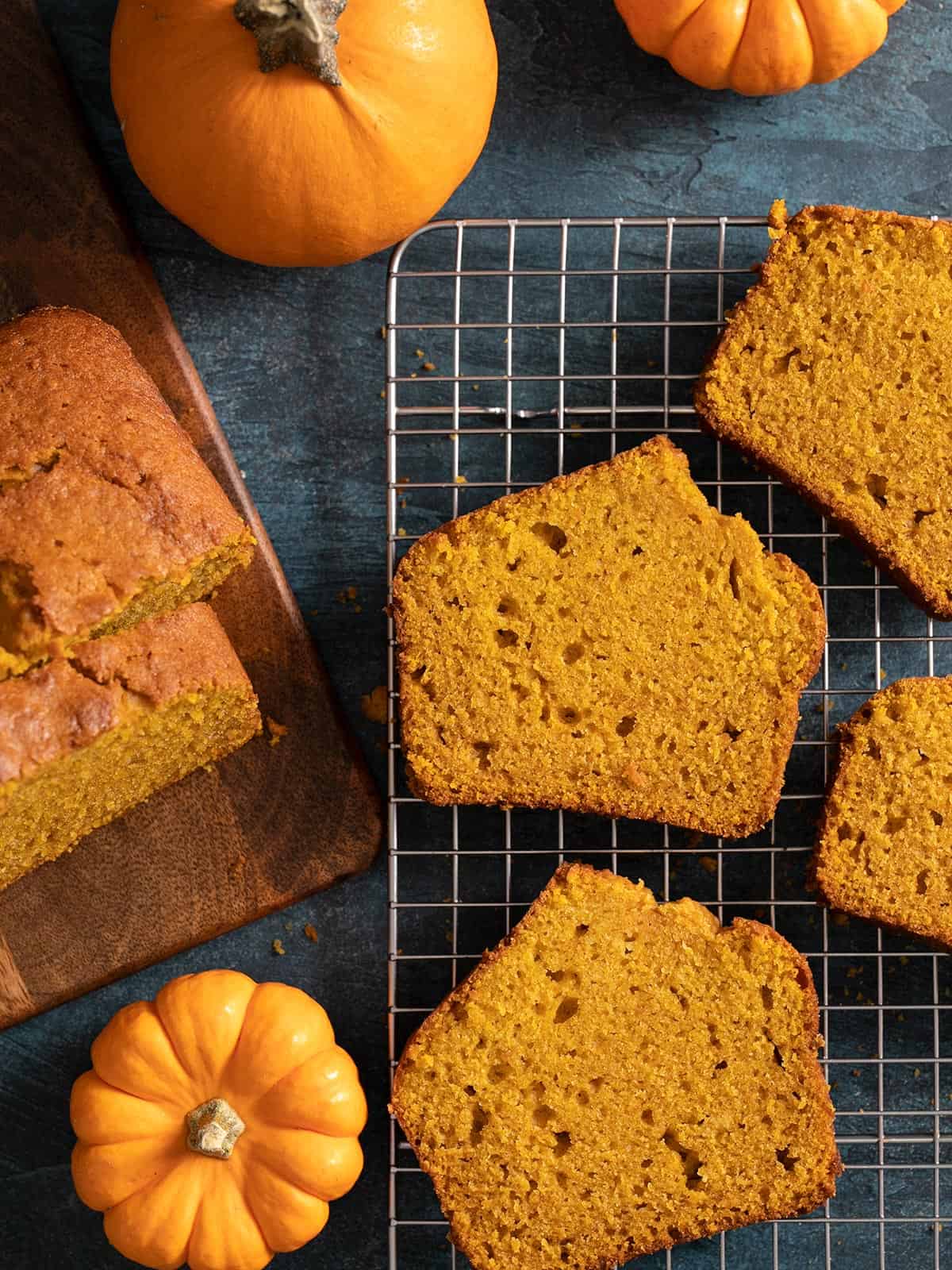 Overhead shot of sliced pumpkin bread with two mini pumpkins next to it on a dark background.