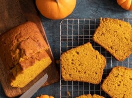 Overhead shot of sliced pumpkin bread with two mini pumpkins next to it on a dark background.