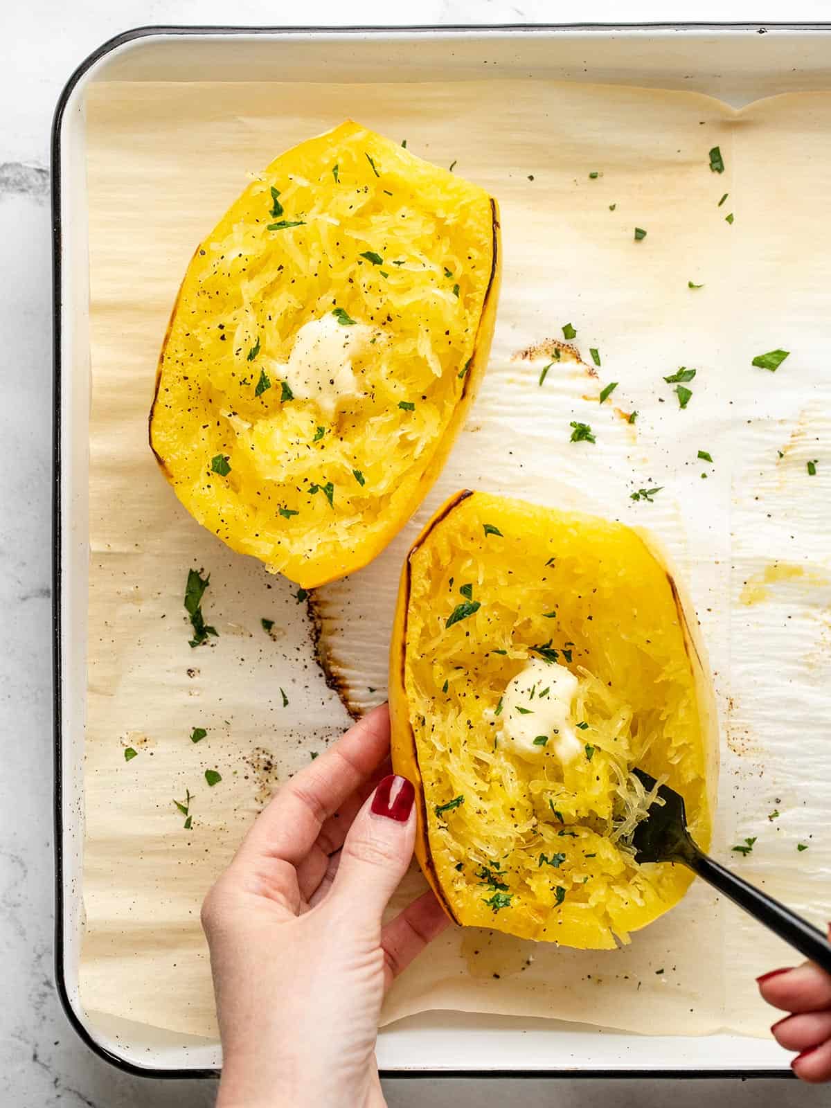 Overhead shot of hand holding cooked spaghetti squash dressed with butter and Italian Parsley. with a fork in it