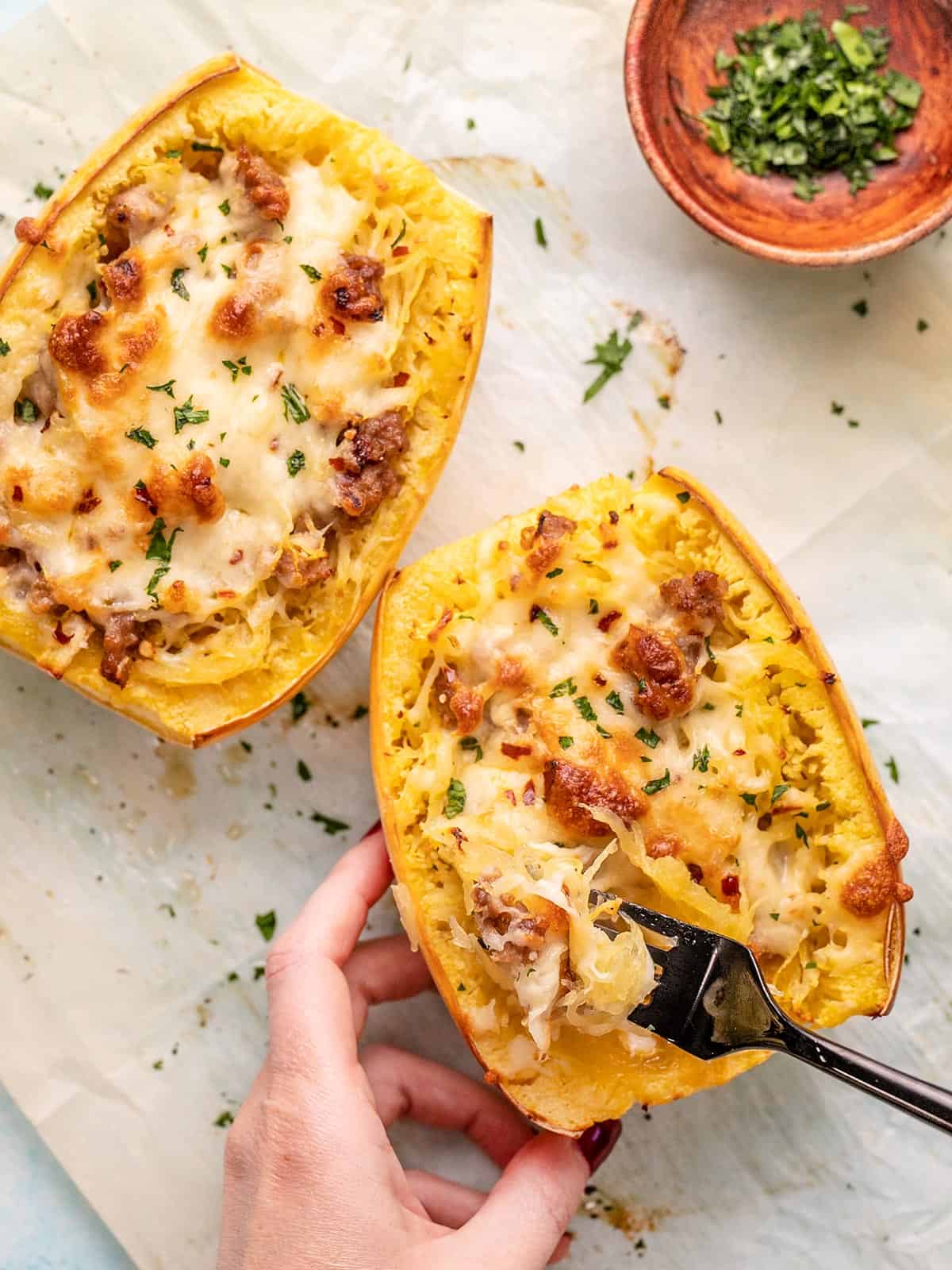 Overhead shot of a hand touching sausage stuffed spaghetti squash with a black fork in it.