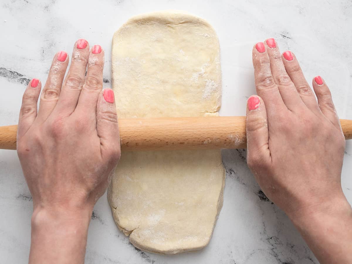 Homemade pie crust being rolled out with a rolling pin. 