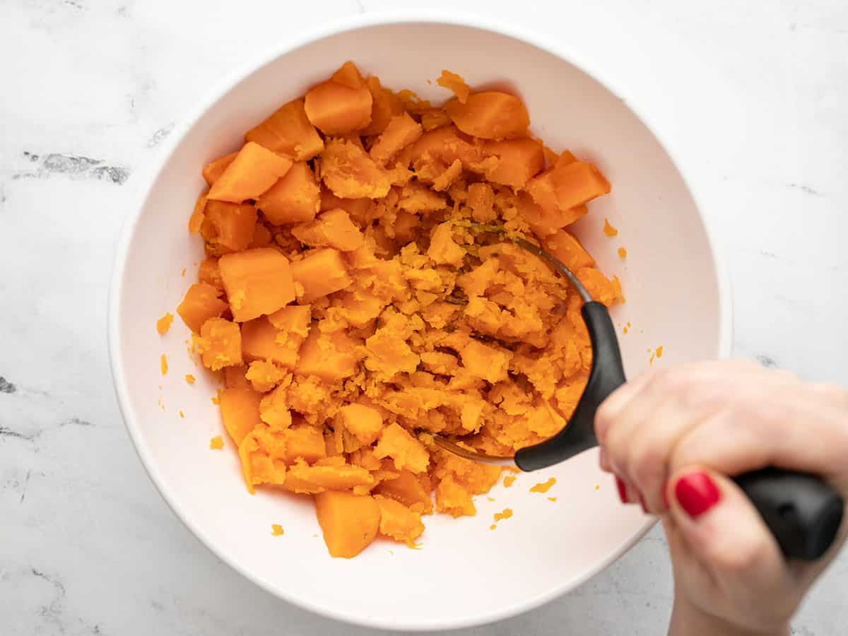 Overhead shot of sweet potatoes being mashed in a white bowl.