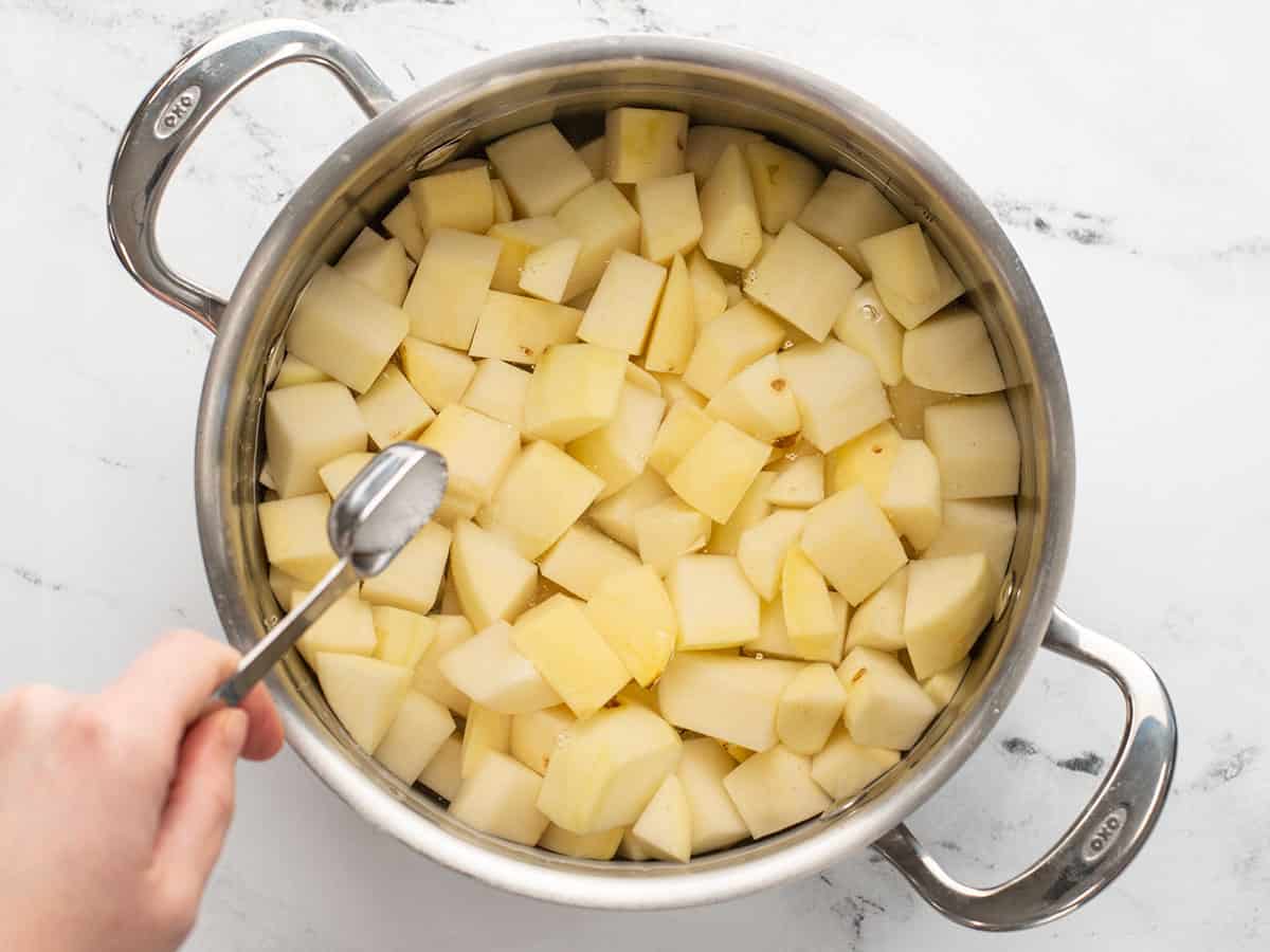 Salt being added to a pot full of potatoes and water.