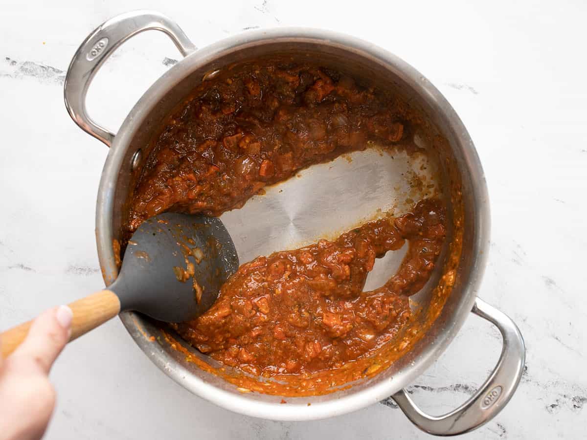 Overhead shot of gray rubber spoon with wood handle scraping the bottom of a silver pot to part sofrito.