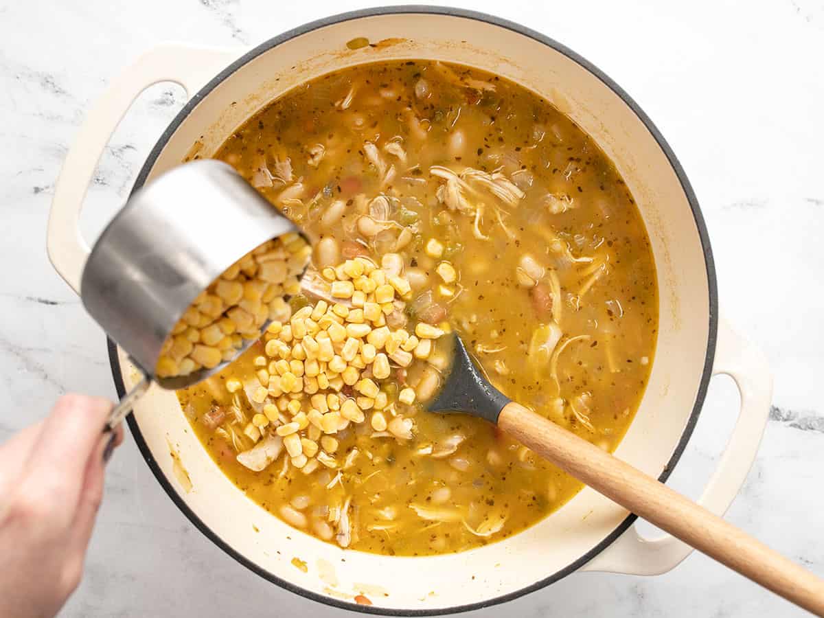 Corn being poured into the chili in the pot. 