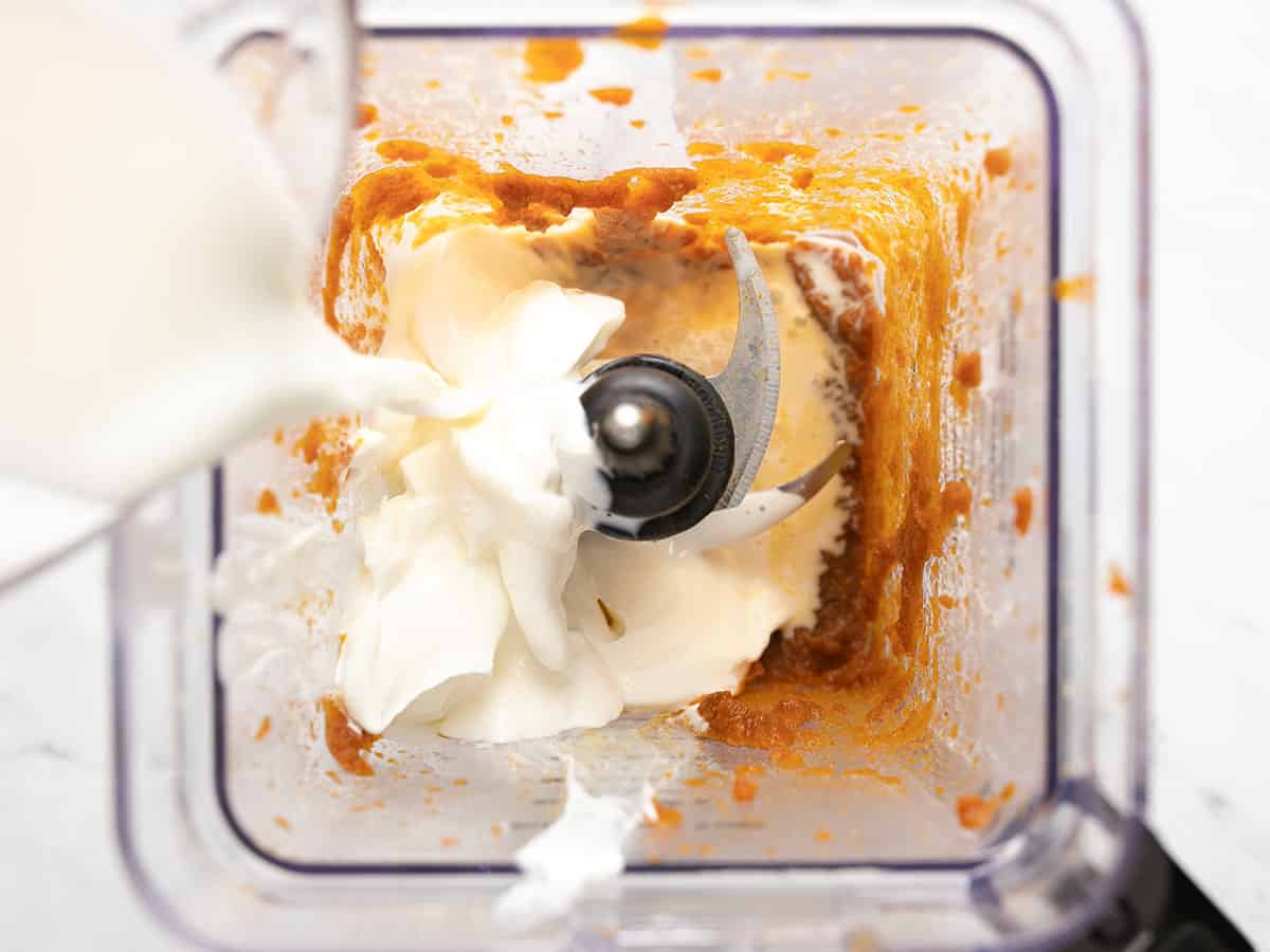 Milk being poured into the blender with pumpkin and spices. 