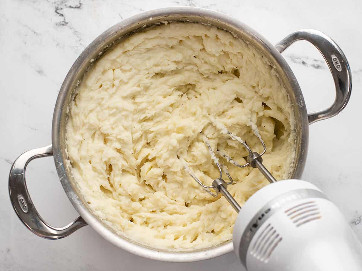 Potatoes being whipped in the pot with a hand mixer.