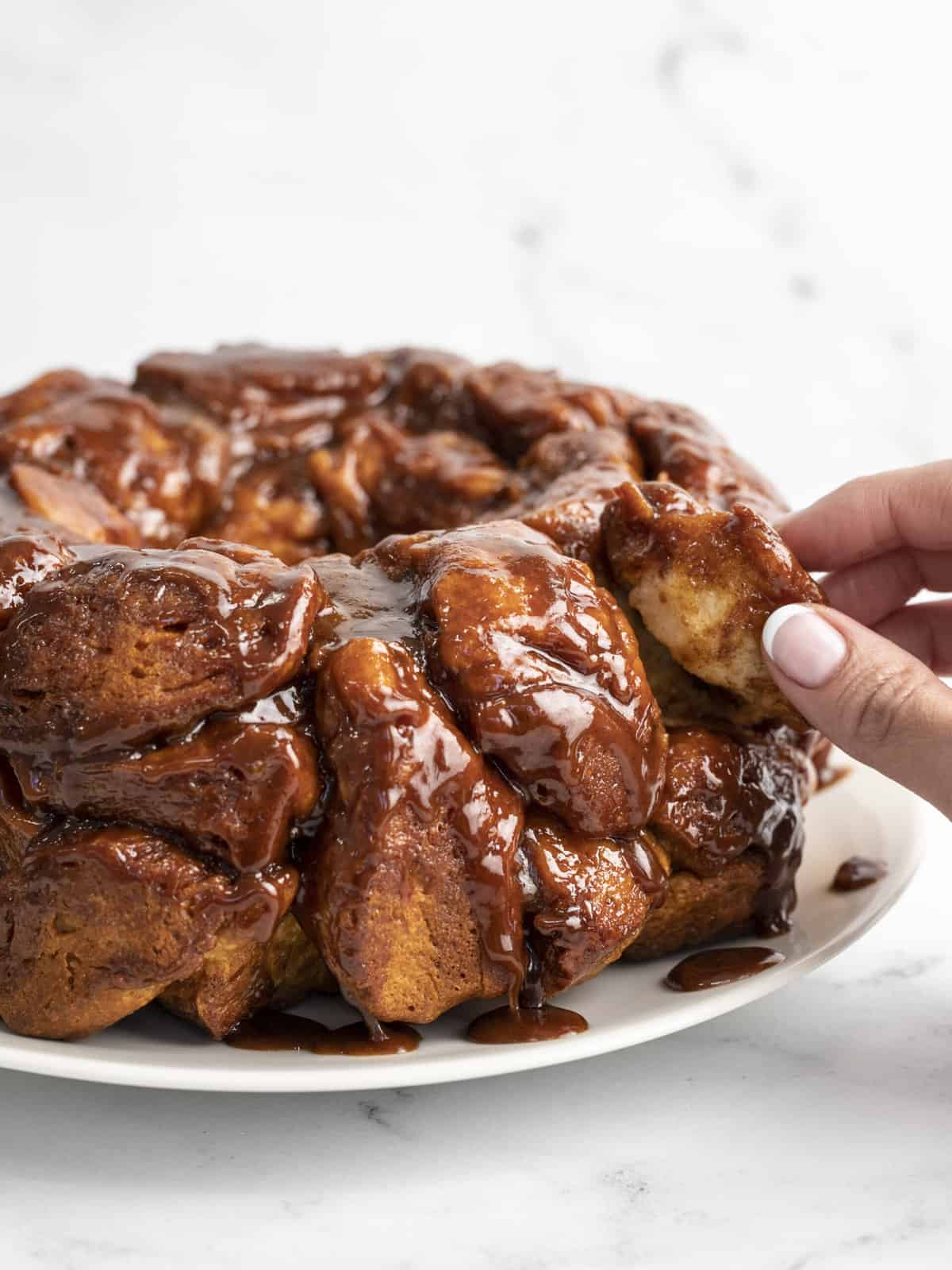 Side shot of hand pulling a piece of monkey bread out of a loaf.