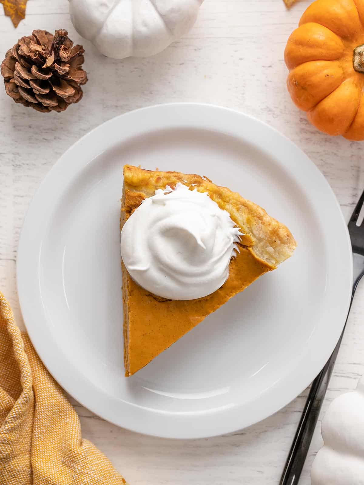 Overhead view of a slice of pumpkin pie with whipped cream on a plate. 