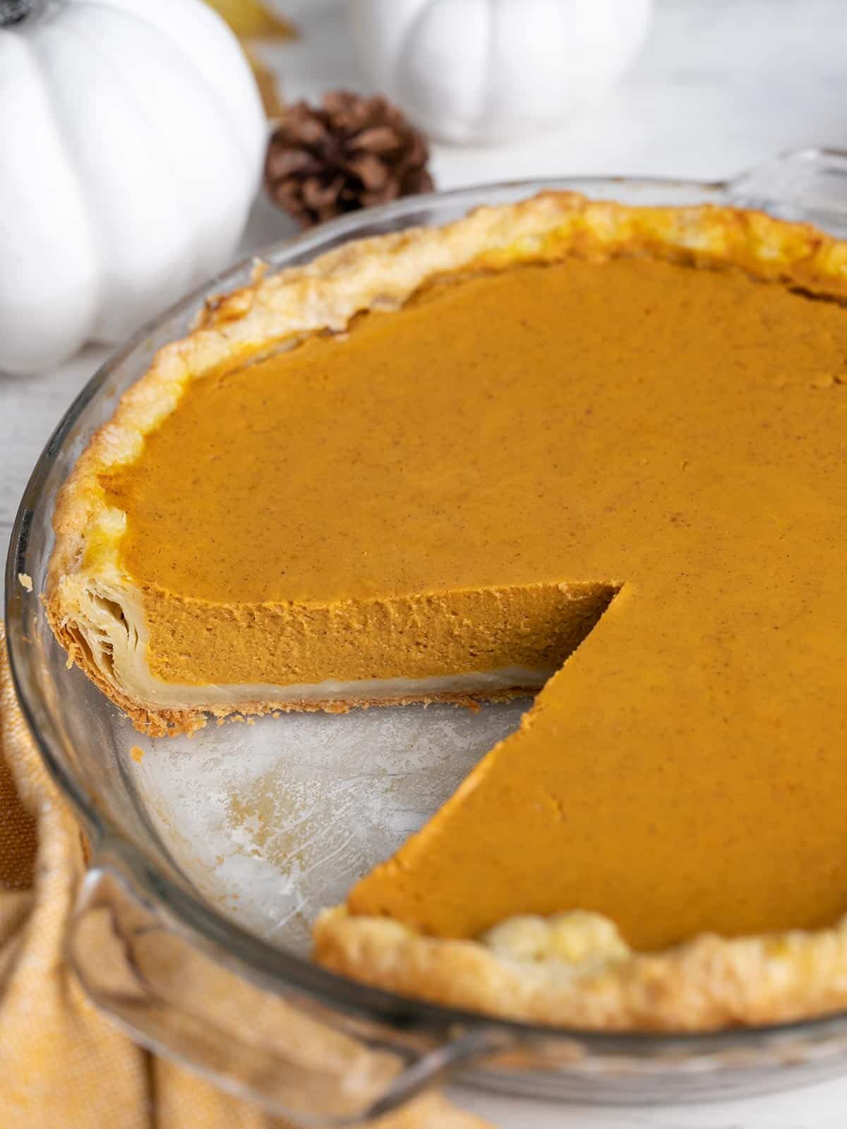 Side shot of a pumpkin pie with a slice taken out of it.