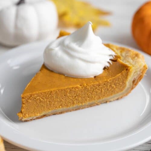 Side shot of a slice of pumpkin pie with a dollop of whipped cream on top of it.