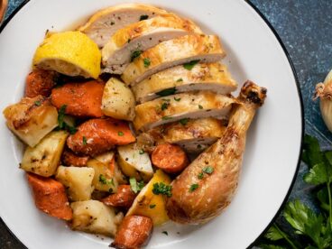 Overhead shot of sliced chicken and roasted vegetables on a white plate.