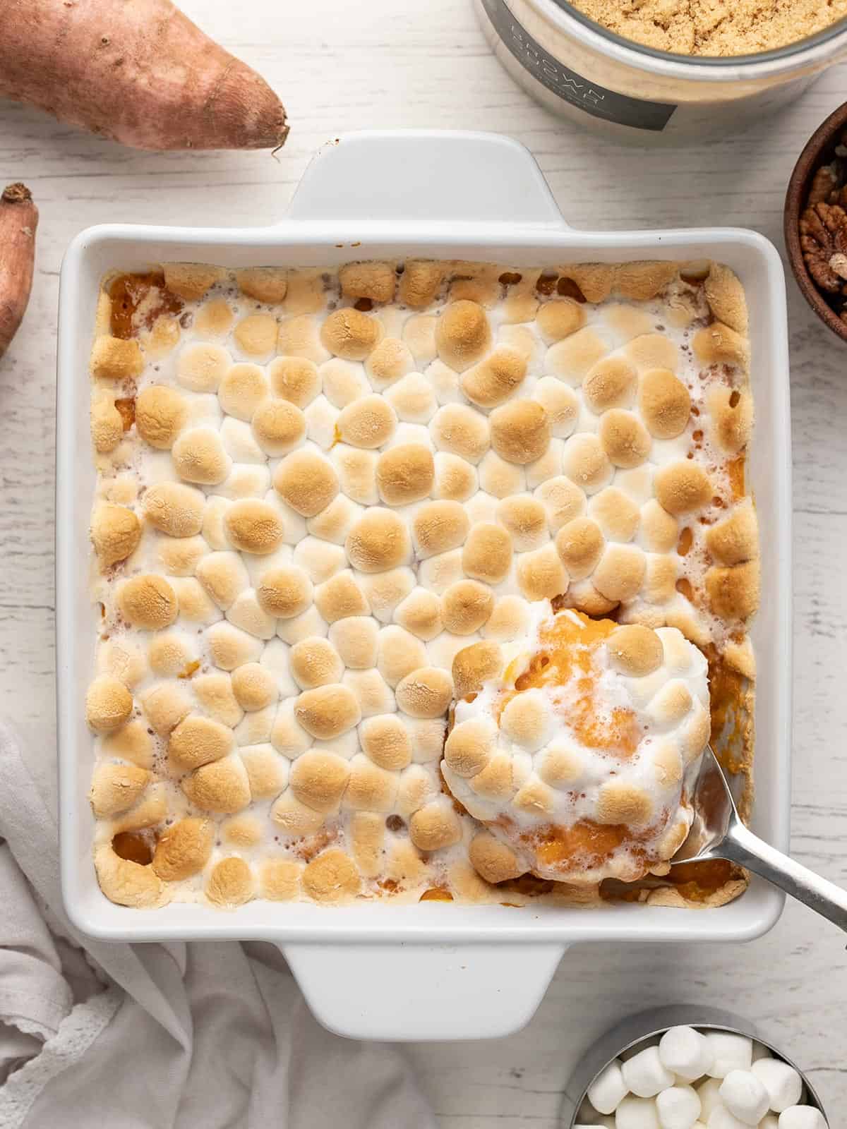 Overhead shot of sweet potato casserole in a white casserole dish with a silver serving spoon scooping out a bit of it.