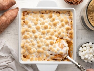 Overhead shot of sweet potato casserole in a white casserole dish with a silver serving spoon scooping out a bit of it.