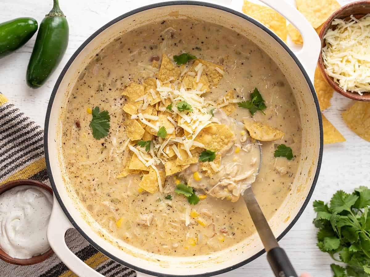 Overhead view of white chicken chili in the pot with toppings and a spoon.