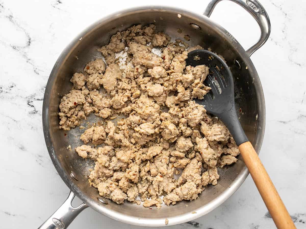 Overhead view of ground chicken browning in a deep-sided skillet.