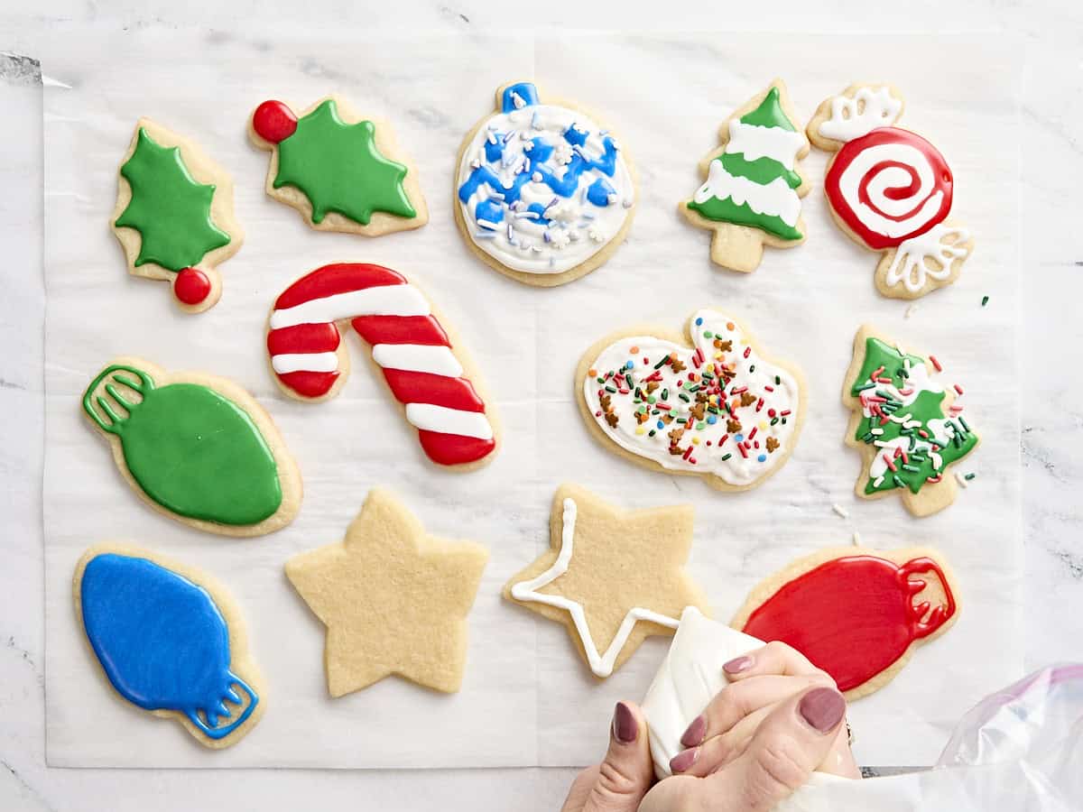 A hand holding a piping bag decorating sugar cookies with royal icing.