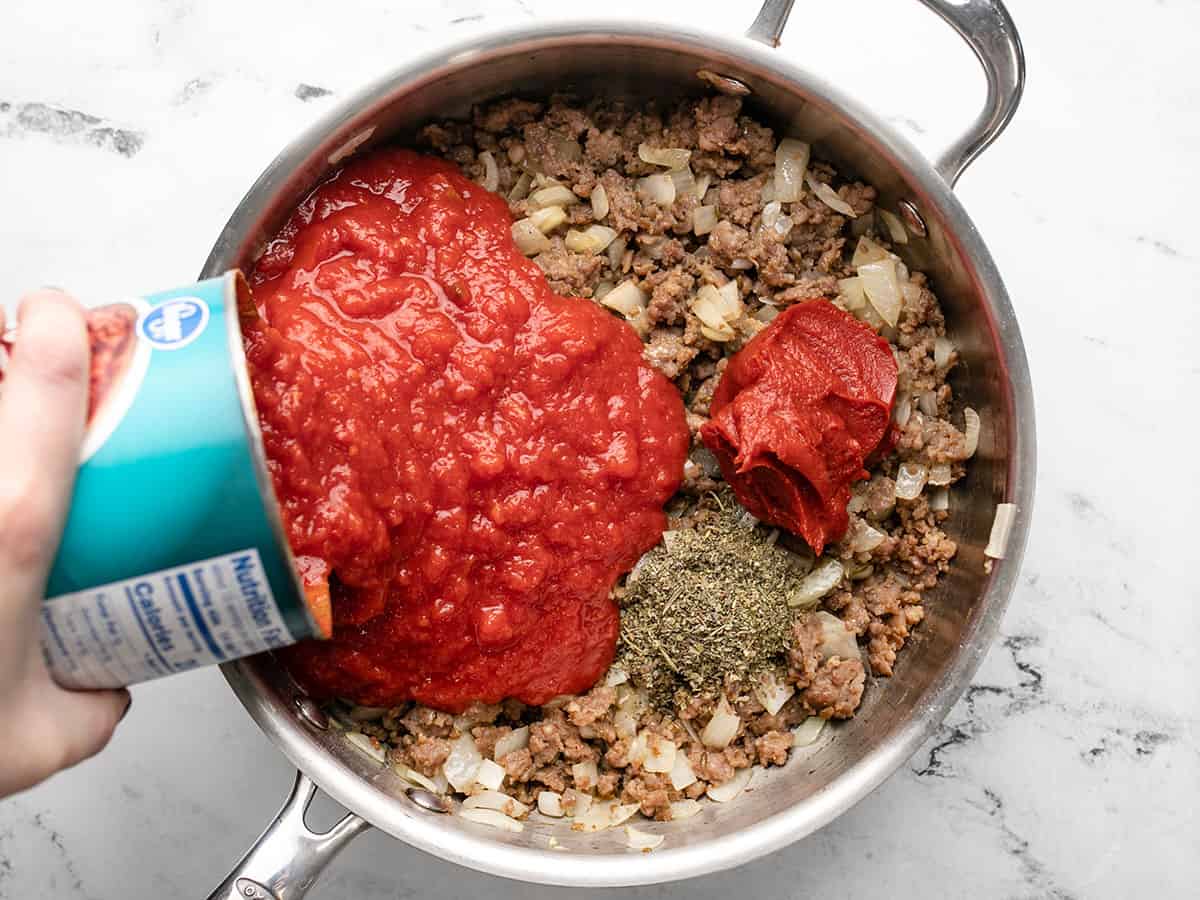 tomatoes and herbs added to meat and onions in the skillet.