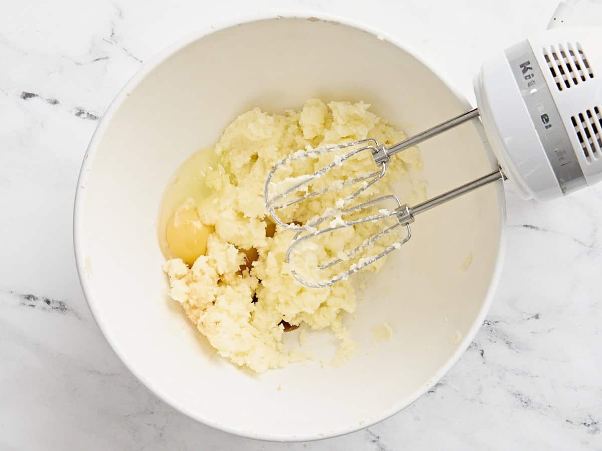 Egg added to creamed butter and sugar mixture in a mixing bowl with a hand mixer.