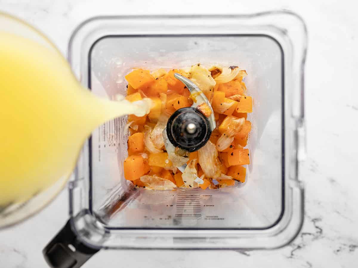 Broth being poured into a blender with the roasted vegetables. 