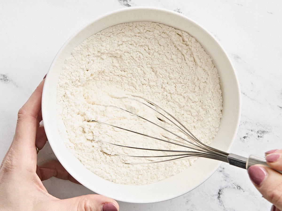 A whisk mixing the dry ingredients for sugar cookies in a mixing bowl.