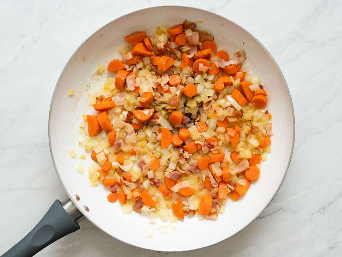 Chopped carrots and onions added to the skillet with the bacon.