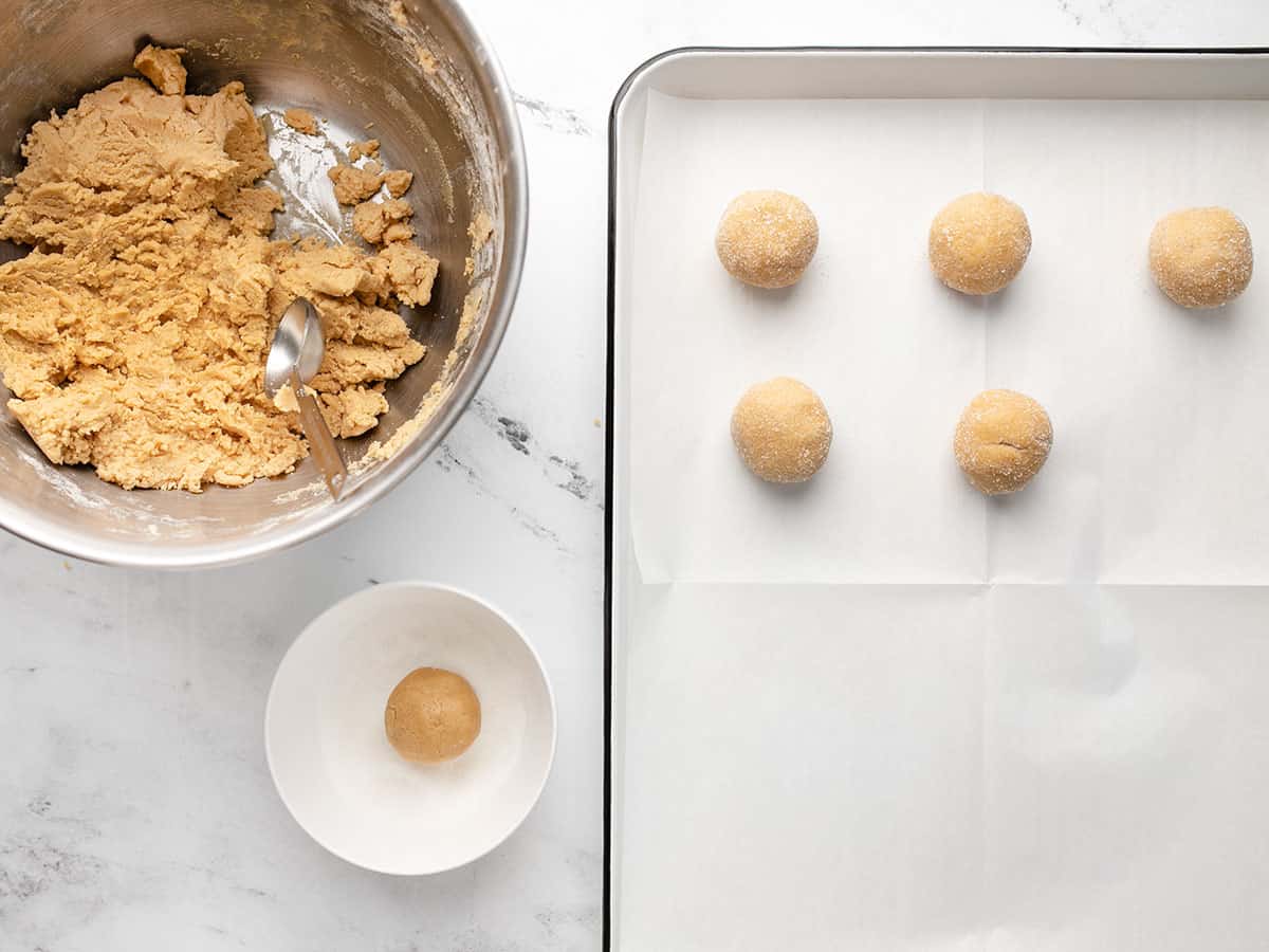 Cookie dough being rolled into balls and coated in sugar.