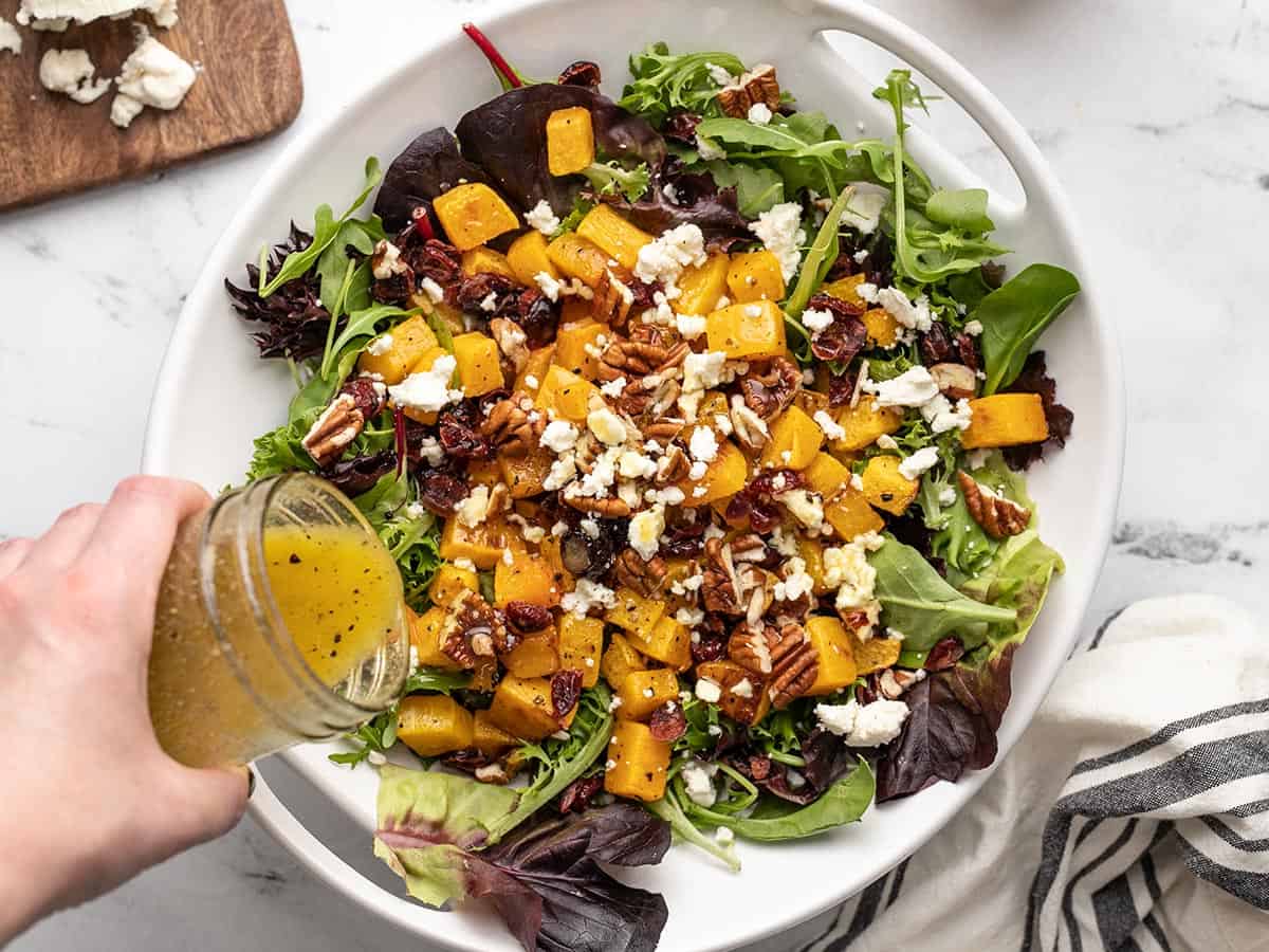 Dressing being poured over the salad in the serving bowl.