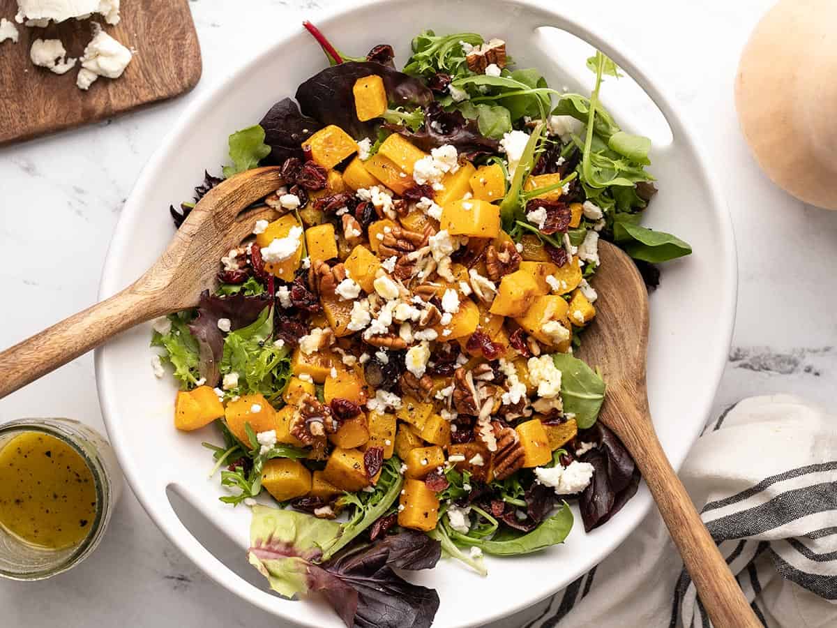 Butternut squash salad in the serving dish with wooden utensiles.