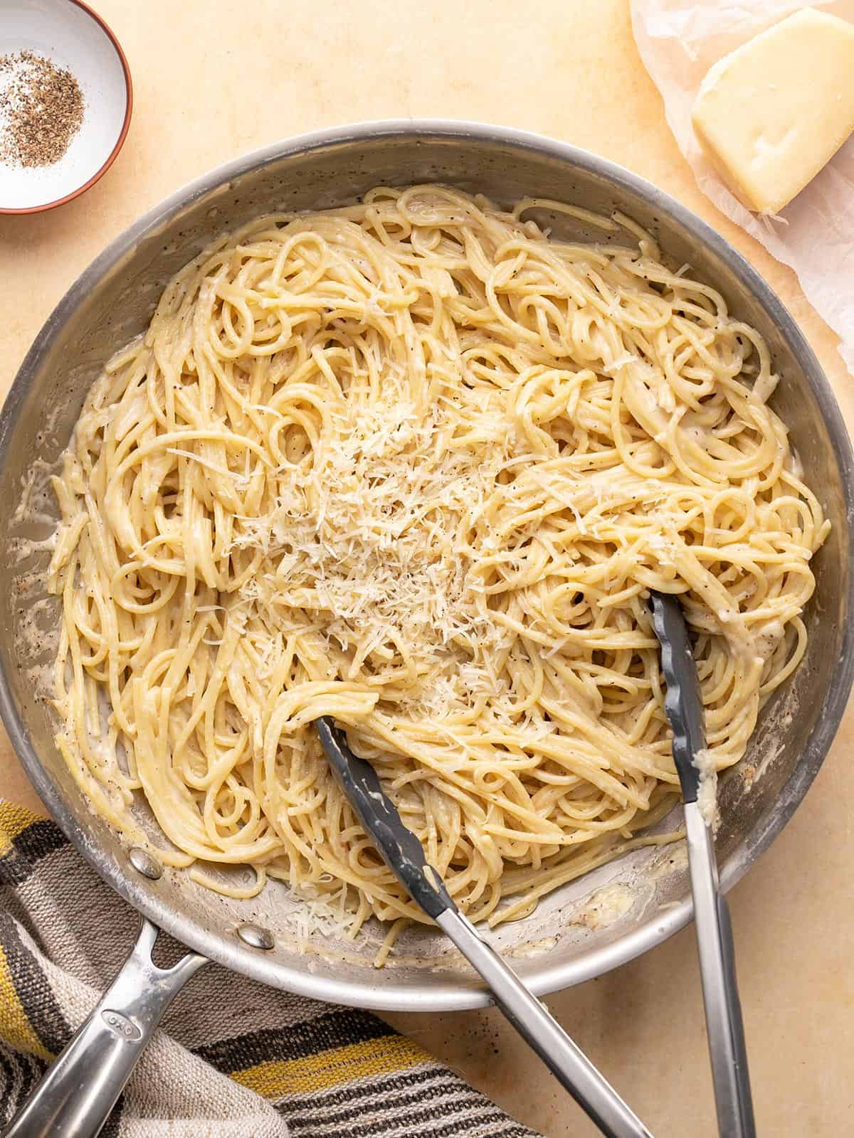 Overhead shot of finished Cacio e Pepe in a pan with tongs in it.