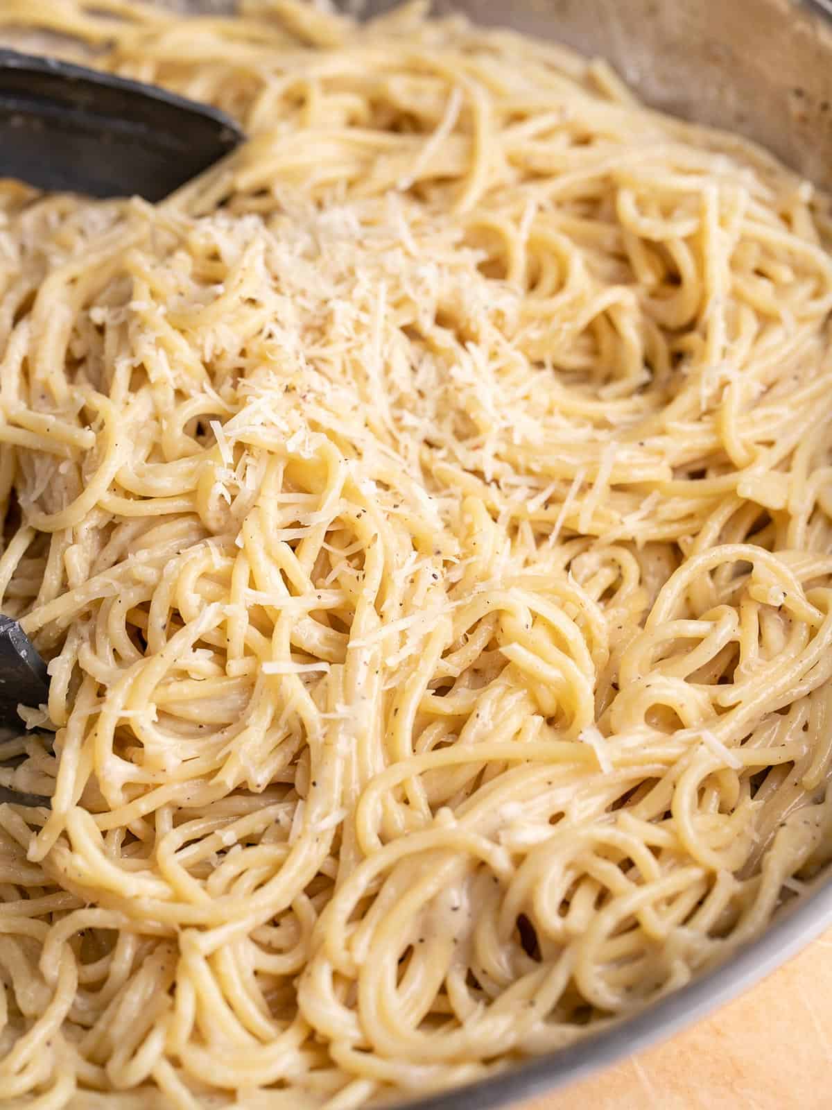 Side shot of finished Cacio e Pepe in a pan with tongs in it.