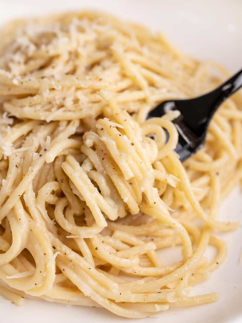 Side shot of finished Cacio e Pepe on a plate with a fork in it.