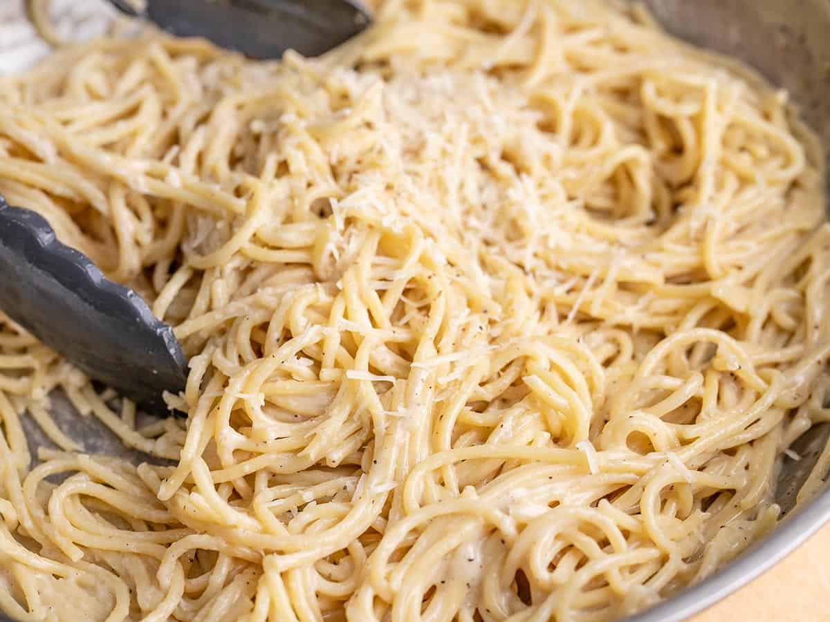 Side shot of finished Cacio e Pepe in a pan with tongs in it.