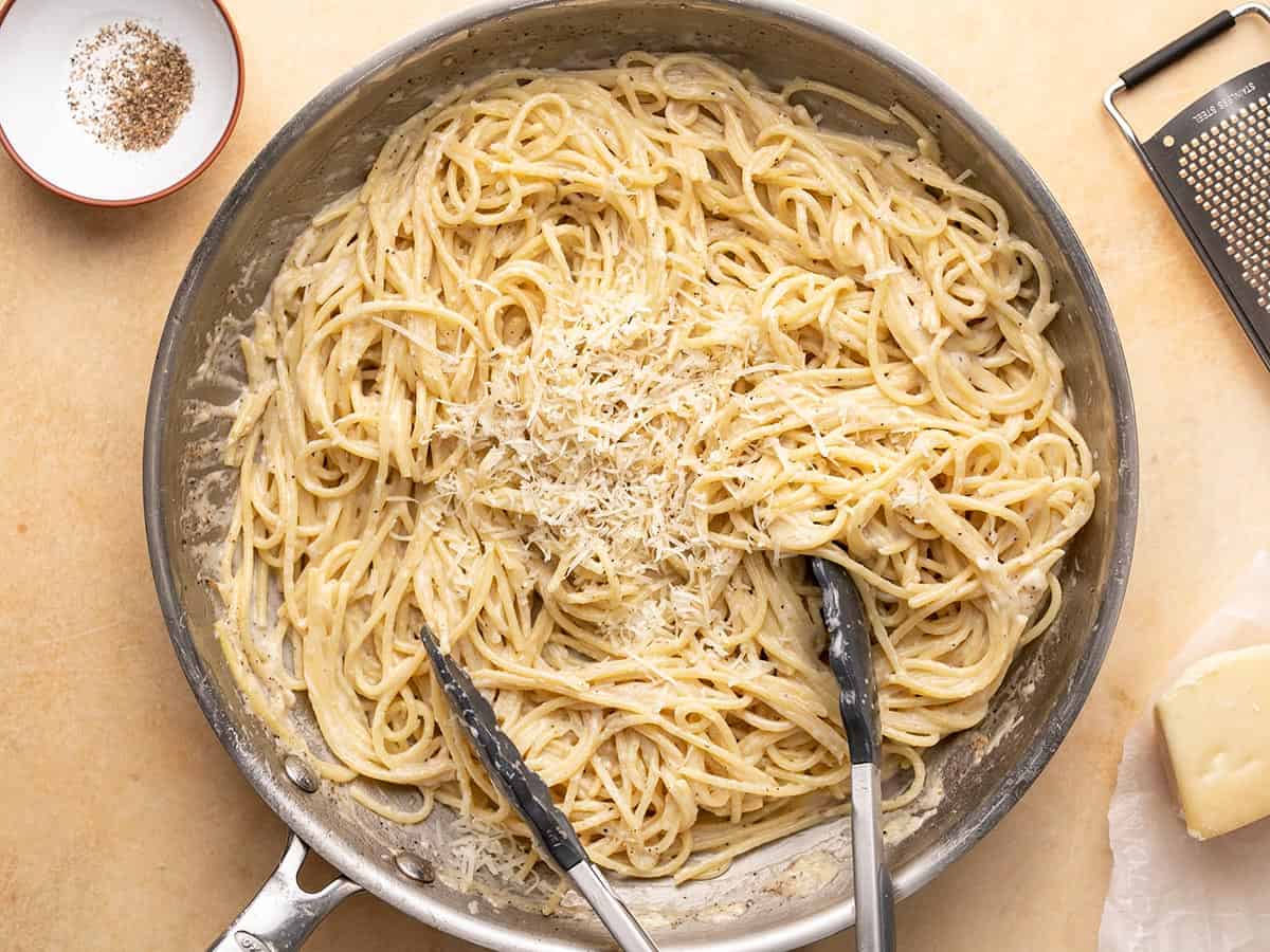 Overhead shot of finished Cacio e Pepe in a pan with tongs in it.