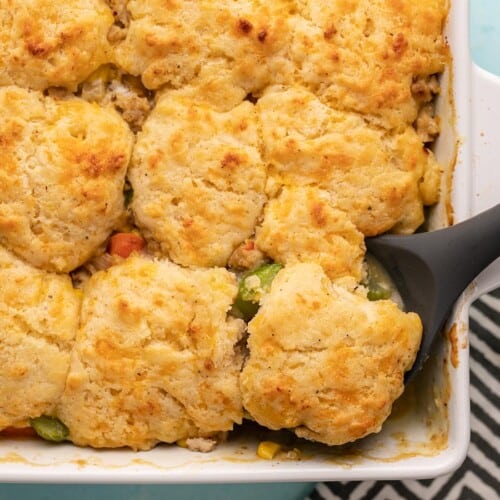 Cooked chicken and biscuit casserole in a casserole dish with a serving spoon.