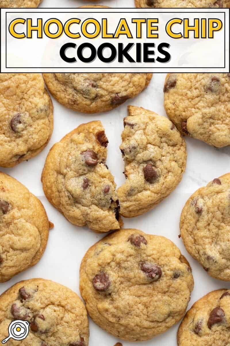 Overhead view of chocolate chip cookies on a white surface, one broken in half.